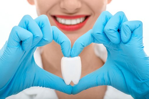 Dental Hygienist holding a fake tooth with her fingers around it in the shape of a heart